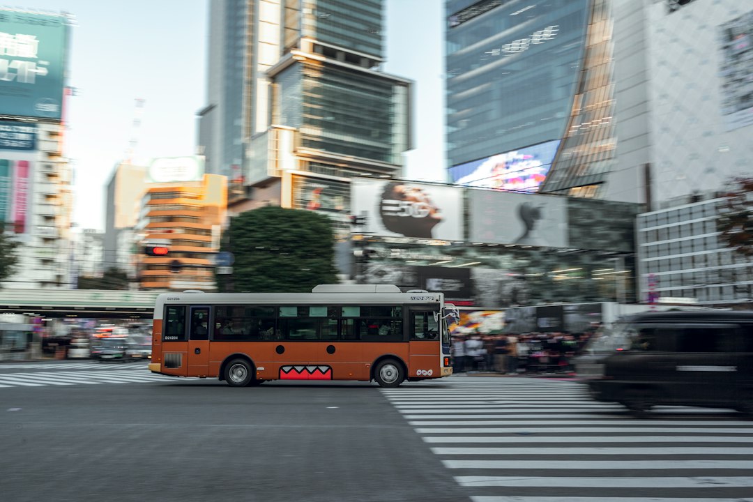 Bus kota berwarna oranye melaju di jalan di antara gedung-gedung tinggi