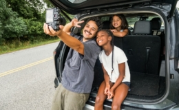 Ayah dan dua anak perempuan berswafoto di samping mobil keluarga